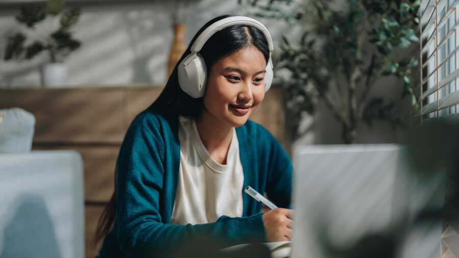 Student taking an online class with headphones and a laptop.